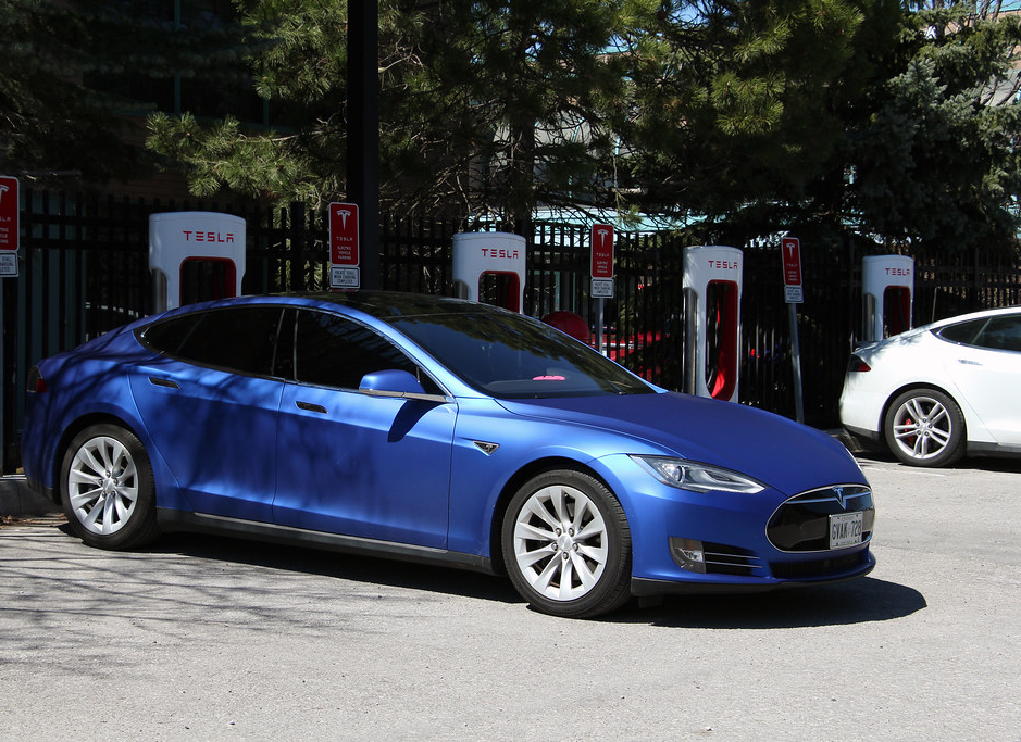 Photo couleur d'une voiture électrique garée à une station de recharge. Panneau de la station : TESLA 