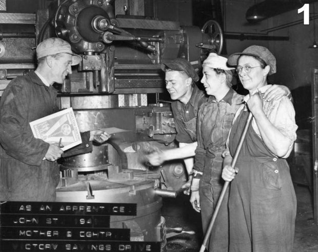 Photographie d'archives en noir et blanc de deux hommes et deux femmes debout devant une grosse machine. La femme au premier plan regarde la caméra et tient un manche à balai. Les hommes et la femme à l'arrière-plan rient et l'un tend un morceau de papier à l'autre. Il y a une impression délavée dans le coin inférieur gauche qui indique AS AN APPRENTICE/JOHN STREET 1941/MOTHER & DAUGHTER/VICTORY SAVINGS DRIVE.