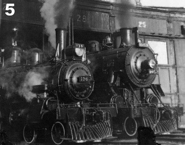 Photo d’archive en noir et blanc de deux locomotives à vapeur sortant d’une rotonde. De la vapeur s’échappe de leurs cheminées et au-dessus des portes des stalles sont inscrits les chiffres 27 et 28.
