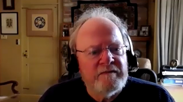 Capture d'écran en couleur d'un homme parlant avec un casque, y compris sa tête et ses épaules. L'arrière-plan montre un bureau.