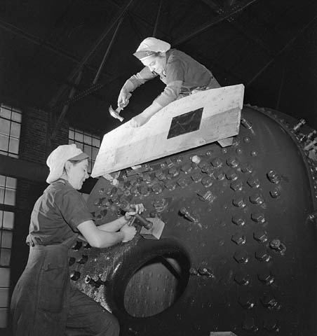 Photo d’archives en noir et blanc de deux femmes en train de travailler sur une grande chaudière de locomotive. Une femme est sur le dessus de la chaudière et martèle le bois qui est fixé à la chaudière. Une deuxième femme est au sol et travaille sur la chaudière.