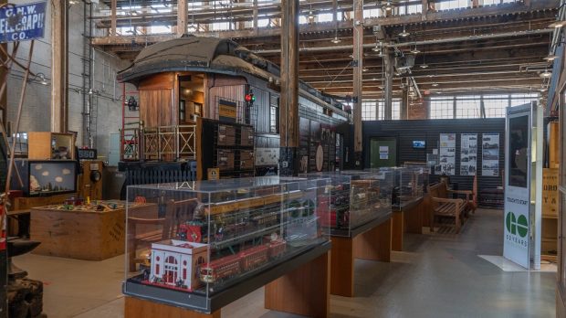 Photographie couleur de l'intérieur d'un musée. Il y a plusieurs vitrines de trains miniatures au premier plan et un wagon de chemin de fer à l'arrière-plan.