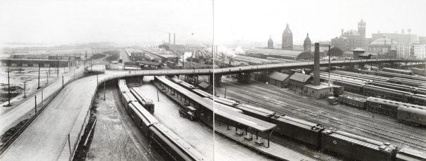 Photographie d’époque en noir et blanc d’un paysage urbain montrant un grand pont au-dessus des voies ferrées. 