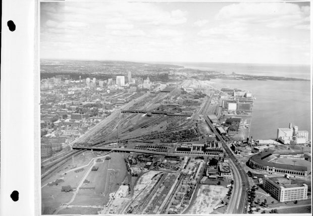 Photographie aérienne d’époque en noir et blanc. Le centre de la photographie montre de nombreuses voies ferrées. Le coin inférieur droit montre un stade de baseball. Le côté gauche de la photographie montre de nombreux bâtiments.