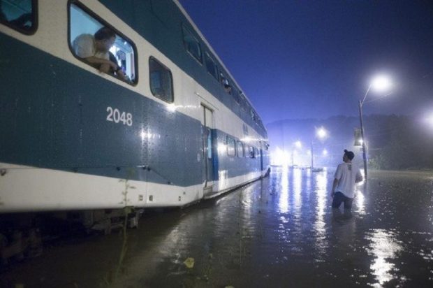 Photographie d’un train GO partiellement submergé dans de l’eau brune. Un passager se penche par une fenêtre ouverte du train. Un homme se tient debout dans l’eau jusqu’aux genoux à côté du train et le regarde.
