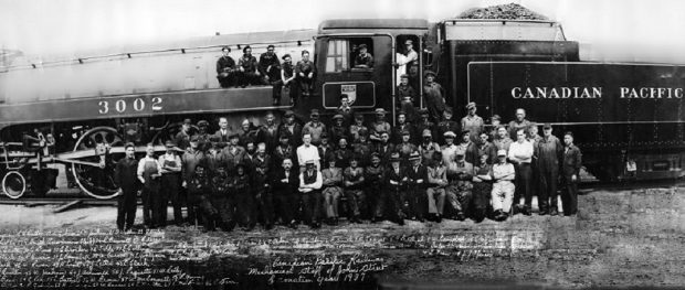 Cette photo d’époque montre environ 50 hommes prenant la pose devant et dans une grande locomotive à vapeur. Le numéro « 3002 » est visible sur la locomotive et « Canadien Pacifique » sur le tender. Une inscription illisible est visible au bas de la photographie.