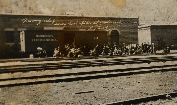  Trois rangées d'hommes devant un bâtiment en brique; première rangée d'hommes sont agenouillés.