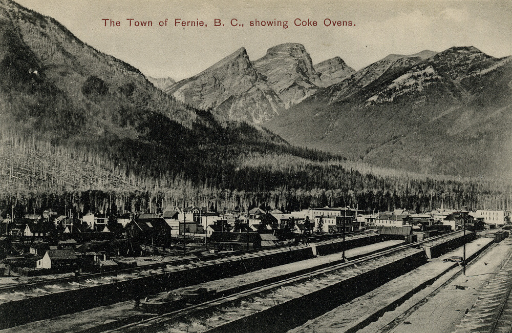  La ville de Fernie avec deux rangées de fours à coke et des voies ferrées à l'avant, des montagnes à l'arrière-plan.