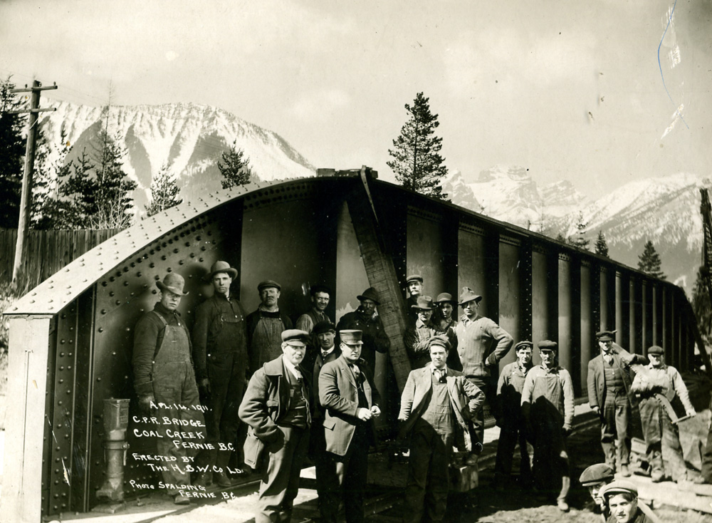 Deux rangées d'hommes debout devant un pont de chemin de fer.