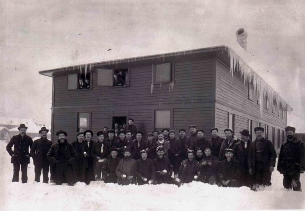 Un grand groupe d'hommes debout devant une maison de deux étages en hiver.