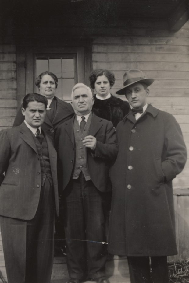  Groupe de trois hommes et deux femmes debout devant une maison.