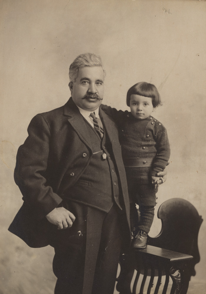 Un homme avec une moustache se tenant à côté d'un jeune garçon sur une chaise.