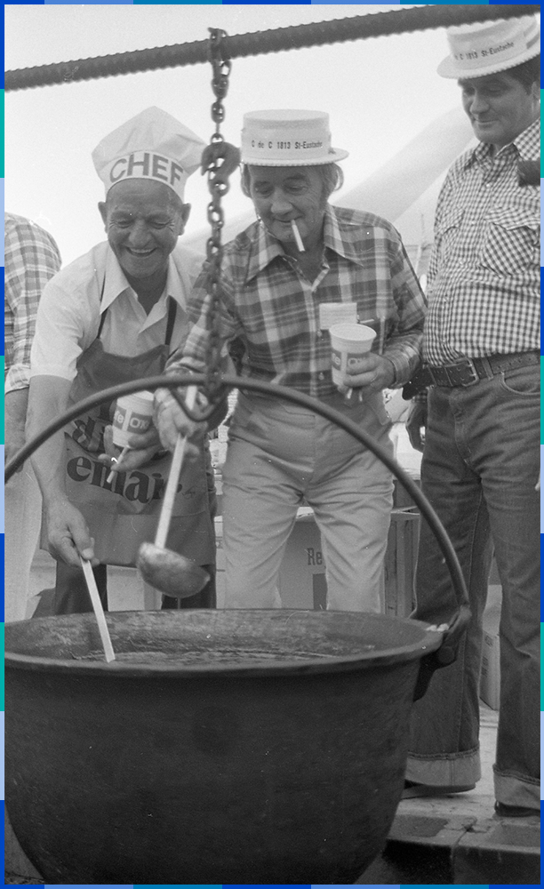 Photographie noir et blanc de trois hommes qui regardent une grande marmite en souriant. Deux d’entre eux tiennent des louches. Le plus vieux des trois porte un chapeau sur lequel on peut lire le mot ‘’chef’’ tandis que les deux autres portent le chapeau des Chevaliers de Colomb de Saint-Eustache.