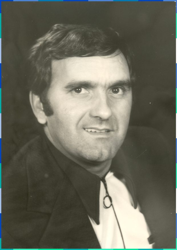 Portrait en noir et blanc d’un homme aux cheveux courts et aux sourcils épais. Il arbore un demi sourire.