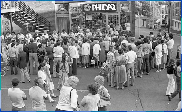 Une vingtaine de femmes, certaines jeunes et d’autres âgées, sont assises en file le long de la rue Saint-Eustache pour tricoter. Devant elles, une foule d’une cinquantaine de personnes les regarde. 