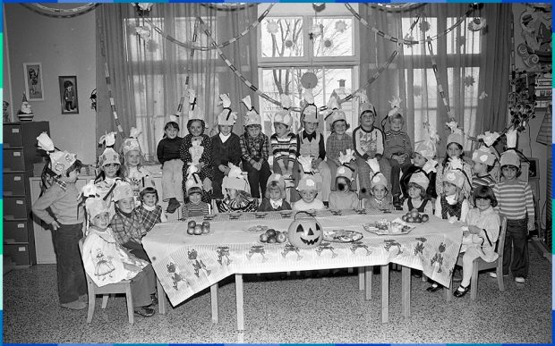 Une trentaine d’enfants d’environ dix ans sont réunis autour d’une table dans une pièce décorée pour l’Halloween. Ils portent tous un chapeau festif. 