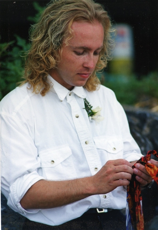 Homme en chemise blanche de style western épinglée d'une rose blanche. Tient un morceau de tissu coloré.