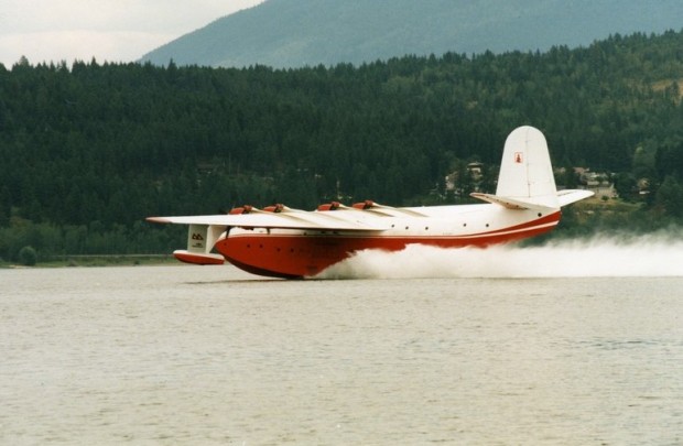 Hydravion rouge et blanc se pose sur l'eau. Colline en arrière-plan.