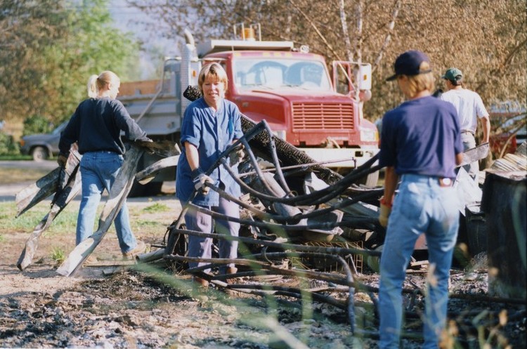 Deux femmes soulèvent du métal tordu d'une pile. Un adolescent transporte du métal vers un camion à benne.