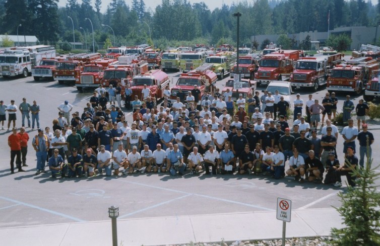 Pompiers assemblés devant des camions de pompiers et des camions-citernes pour une photo de groupe.