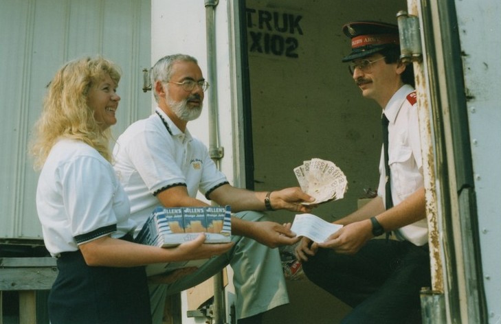 Homme et femme offrent plusieurs billets de $100., un chèque et des boîtes de jus à un officier de l'Armée du Salut.