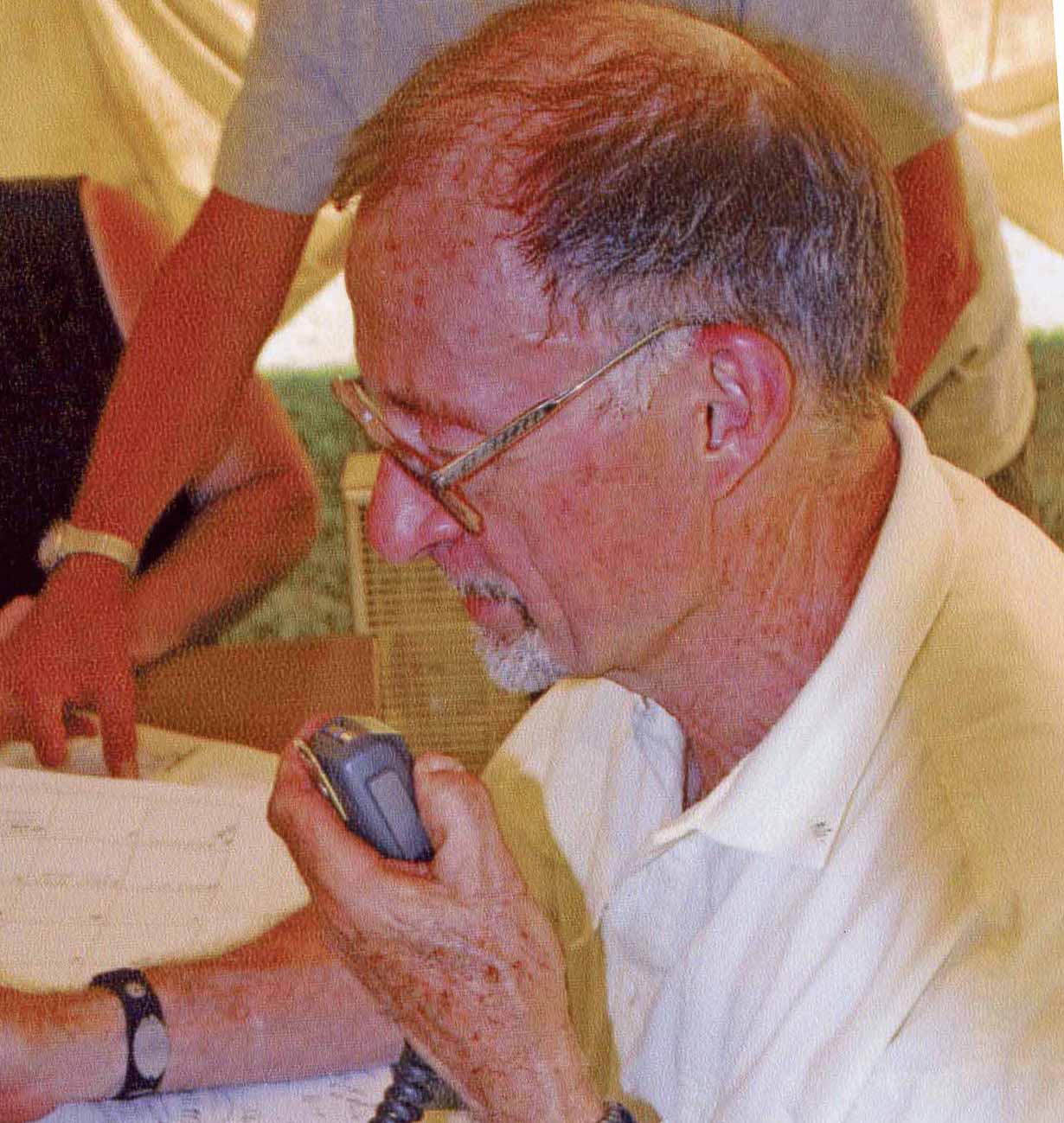 Homme avec barbichette et lunettes  parle dans un radiotéléphone.
