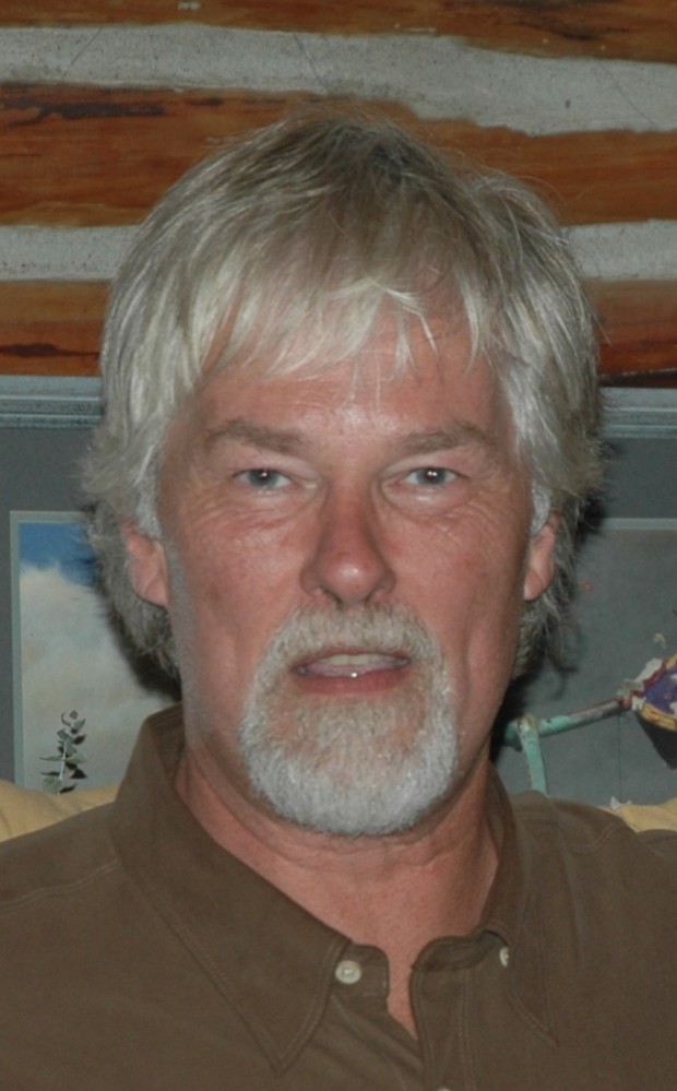Homme aux cheveux gris avec barbiche regardant vers la caméra.