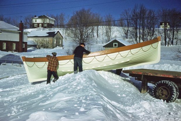 Photographie couleur où deux hommes, un jeune et un âgé, glissent une chaloupe blanche sur un amas de neige afin de l’installer sur la plate-forme arrière d’un camion.