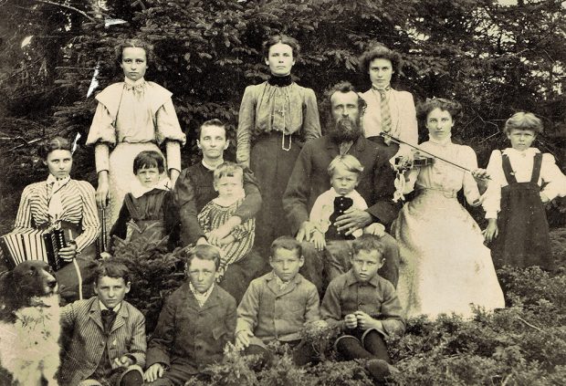 Photographie noir et blanc montrant les parents de François-Xavier Lachance, leurs 13 enfants et leur chien. Tous regardent la caméra, assis ou debout devant un boisé.