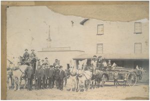 Homme debout devant un moulin avec un carrosse décoré et un cheval.