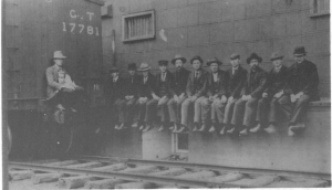 12 hommes assis sur un banc près d’un train.