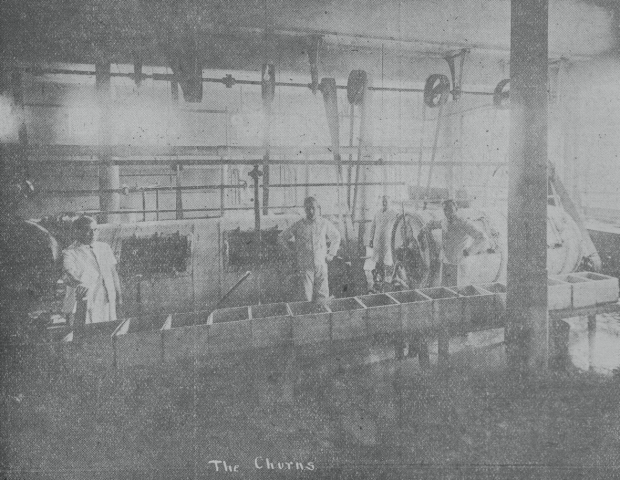 Photographie en noir et blanc de quatre hommes derrière des caisses de beurre.