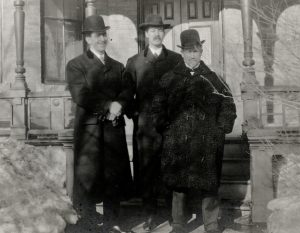 Trois hommes debout devant un escalier portant des manteaux d’hiver.