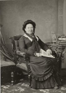 Photographie de studio d’une femme assise sur une chaise qui porte une robe noire.