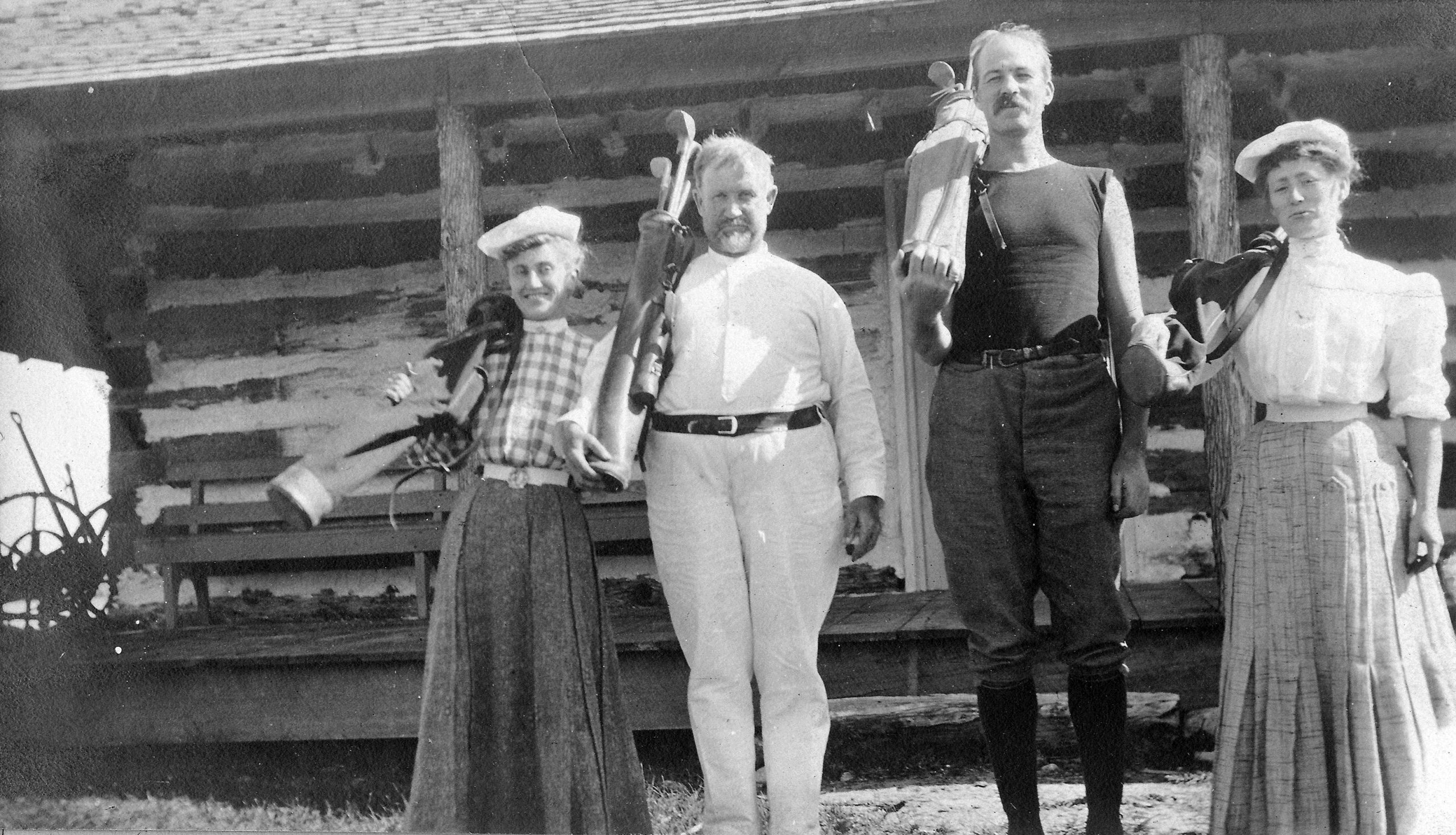 Deux femmes et deux hommes qui tiennent des bâtons de golf devant une cabane de bois.
