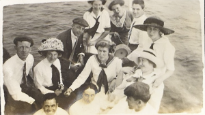 Groupe de jeunes hommes et femmes habillés en robes blanches et complets noirs à bord d'un bateau. 