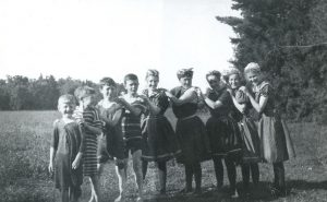 Une rangée de neuf enfants sur la pelouse qui portent des costumes de bain. 