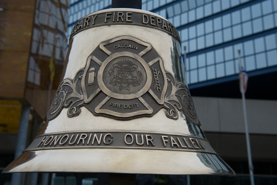 Sur ce gros plan de la cloche en argent, on aperçoit le nom du service d’incendie de Calgary gravé en hommage à ses pompiers disparus, avec insigne gravé du service d’incendie. On aperçoit l’hôtel de ville en arrière-plan