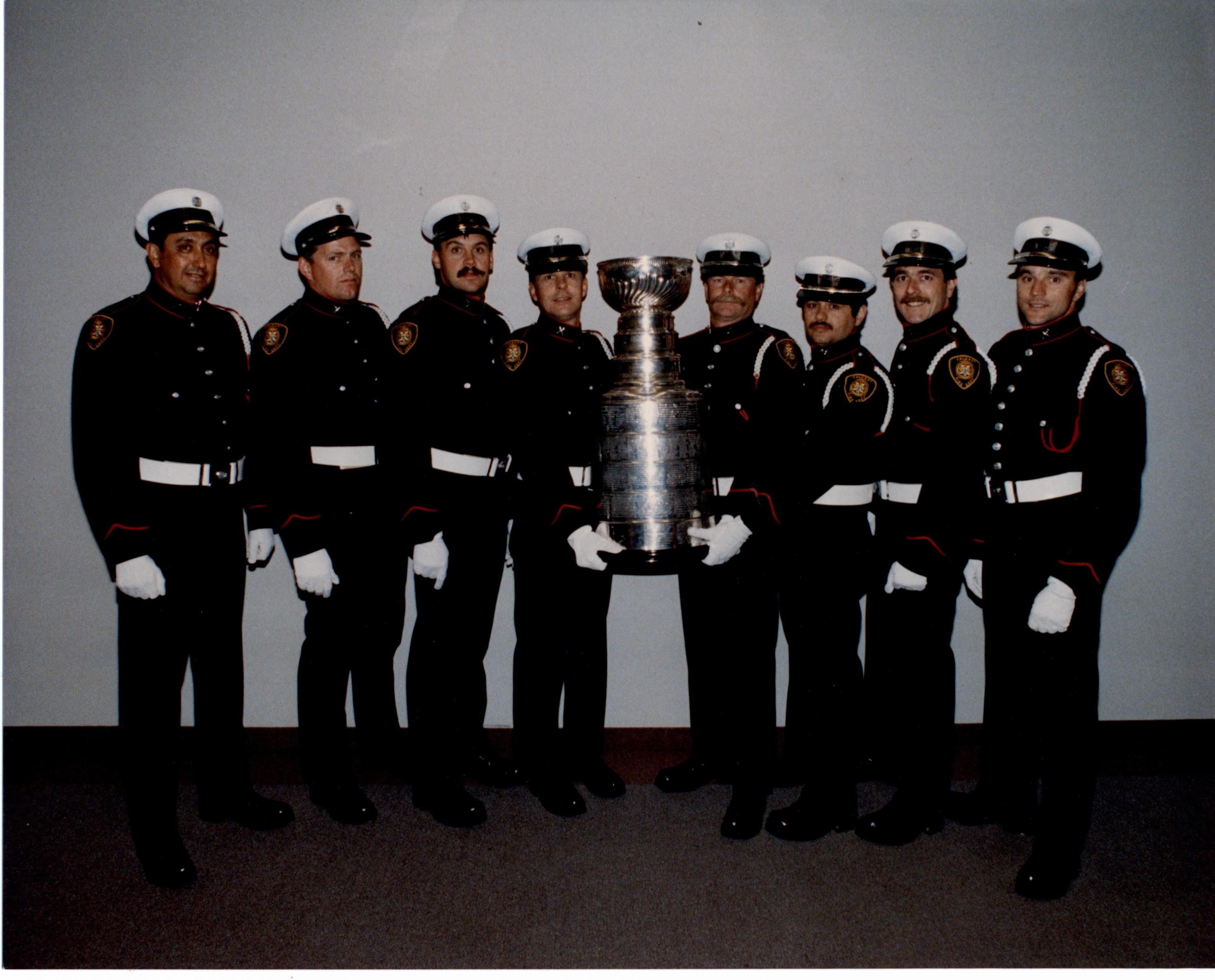 Huit pompiers en uniforme, de part et d’autre de la Coupe Stanley, au centre