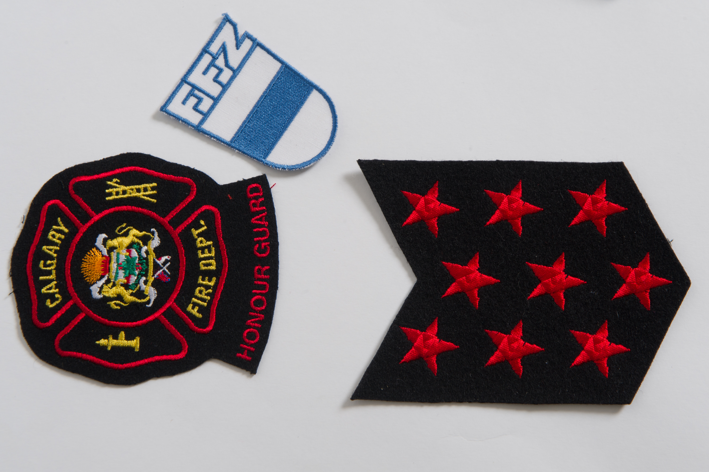 Trois insignes : l’insigne du service d’incendie de Calgary avec le logo de la ville, les neuf étoiles rouges et un insigne blanc et bleu du service d’incendie bénévole de la ville natale de Tobias Breuer (FFZ), en Suisse