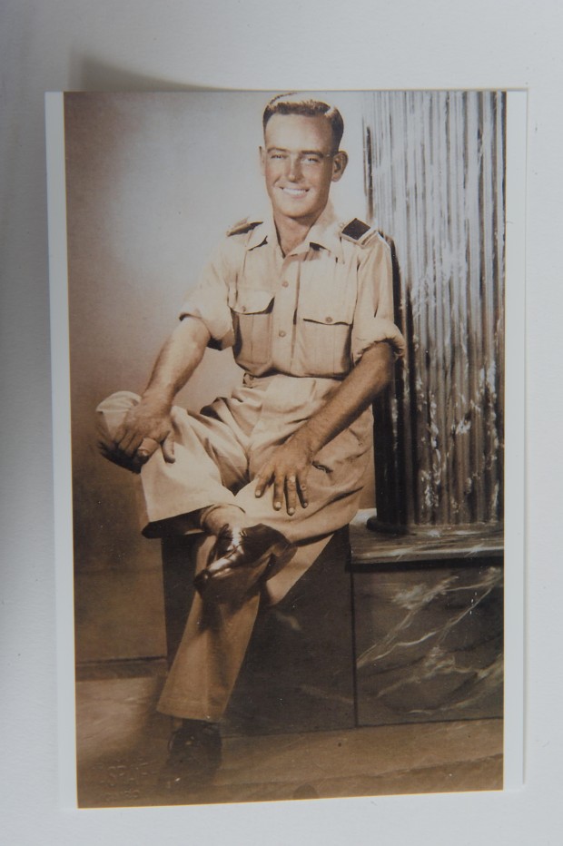 Sur cette photo sépia, on aperçoit un homme en uniforme militaire, assis de manière décontractée, la jambe droite sur le genou gauche, les manches de chemise retroussées, les deux mains sur les genoux.