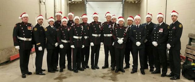 Dix-sept pompiers en uniforme de grande tenue, souriant dans les coulisses, avec chapeau rouge de père Noël