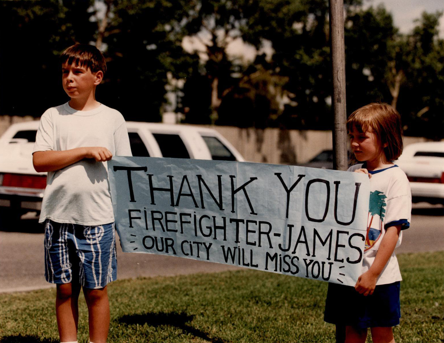 Deux enfants tiennent une bannière sur le trajet du cortège funèbre. « Merci, pompier James. Vous allez manquer à notre ville. »