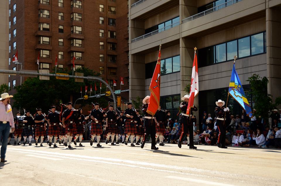 La garde d’honneur défile au centre-ville avec les drapeaux du service d’incendie, du pays et de l’union au Stampede de 2015. Elle est suivie des membres des Pipes and Drums en jupe écossaise rouge.