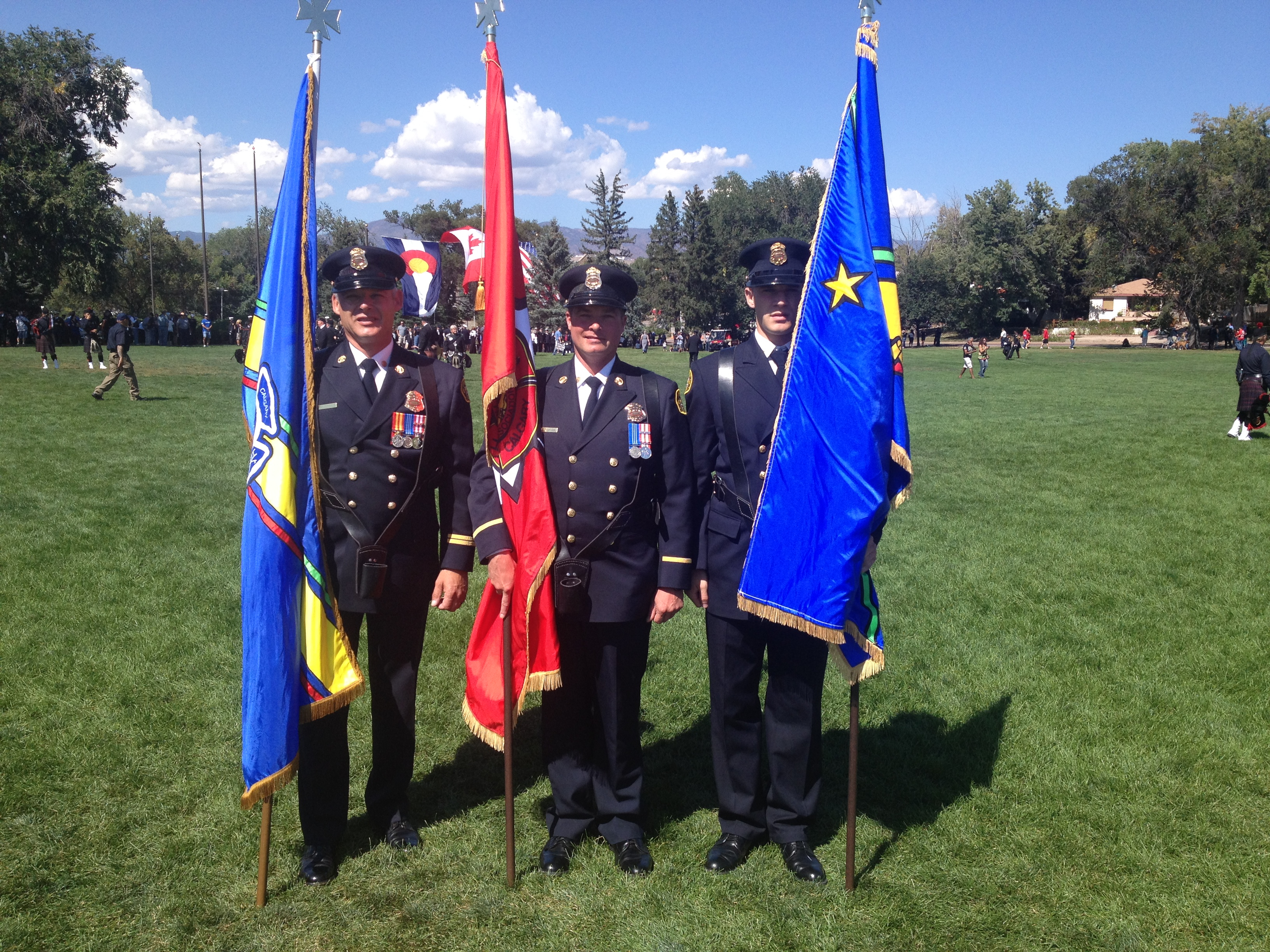 Trois membres de la garde d’honneur en uniforme de grande tenue sur la pelouse, portant tous un drapeau différent