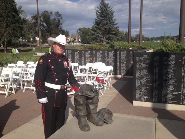 Un garde d’honneur du service d’incendie de Calgary en uniforme et chapeau de cowboy blanc à côté de la sculpture d’une paire de bottes, devant le mur commémoratif portant le nom des pompiers disparus