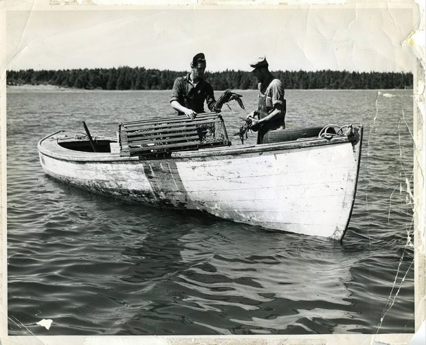 Photo noir et blanc de deux hommes sur un bateau avec des homards et des nasses.