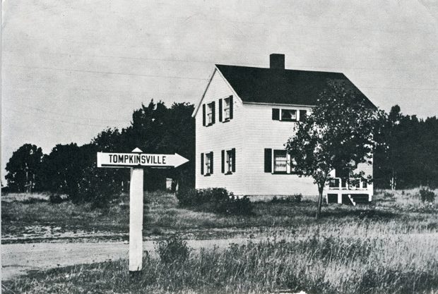Photo noir et blanc d’une maison blanche et d’une pancarte en direction de Tomkinsville.