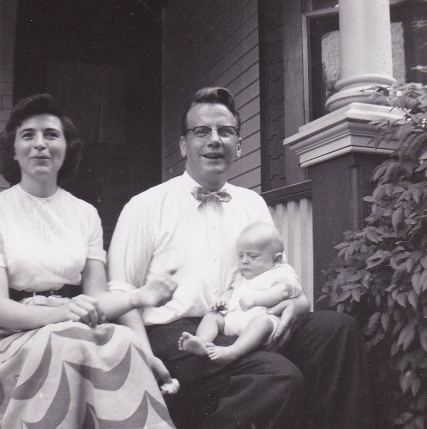 Un homme et une femme assis côte à côte dans la véranda d’une maison ; le père tient le bébé sur ses genoux.