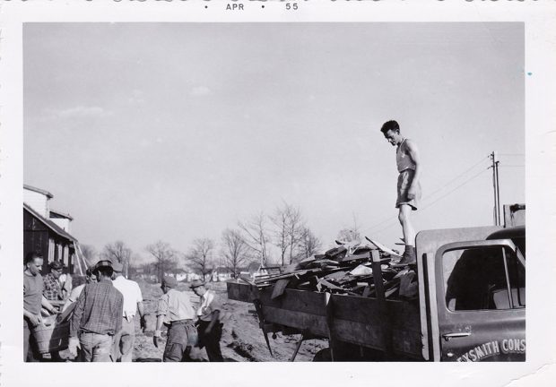 Photo noir et blanc d’hommes déchargeant un camion ; en haut est tapé à la machine APR 55.